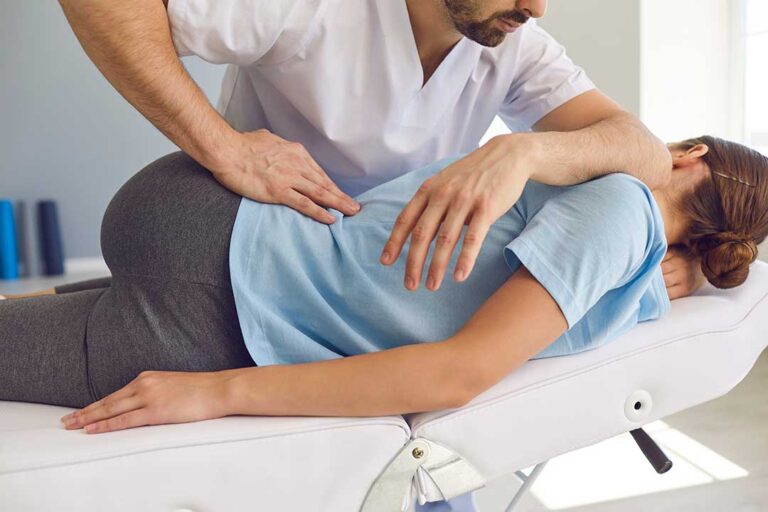 A chiropractor examines a young athlete’s knee on a padded table in a bright, welcoming clinic.
