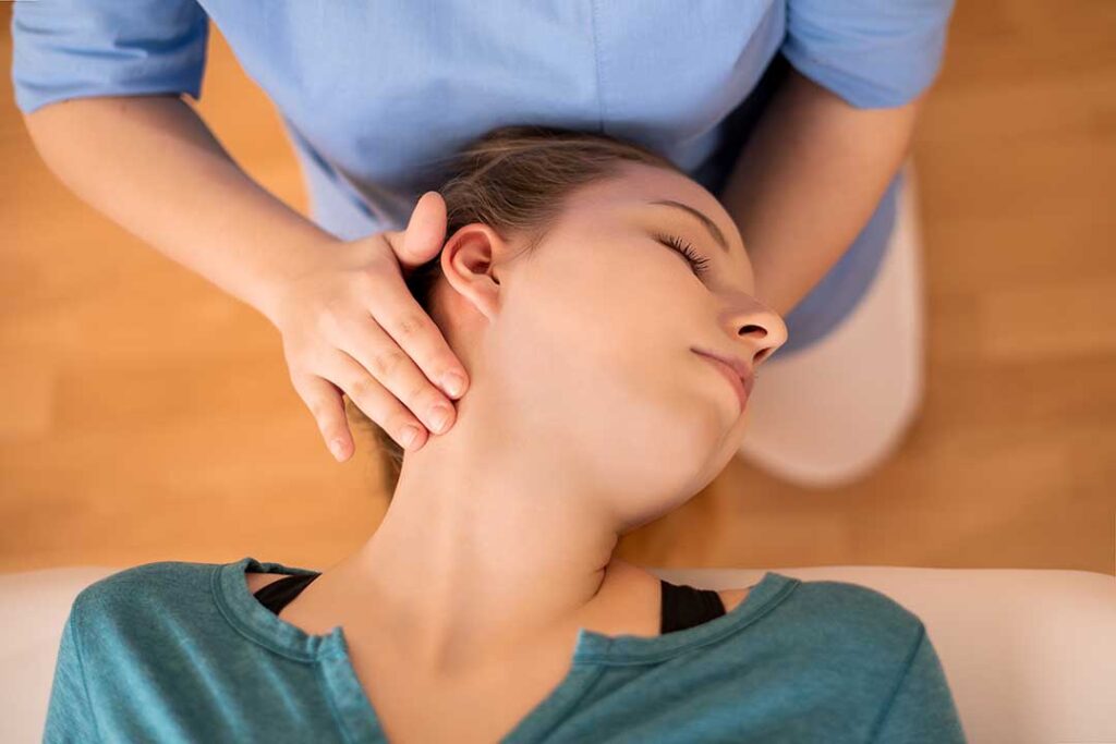 A person performs gentle back mobility exercises on a mat beside a clinician in a bright wellness room.