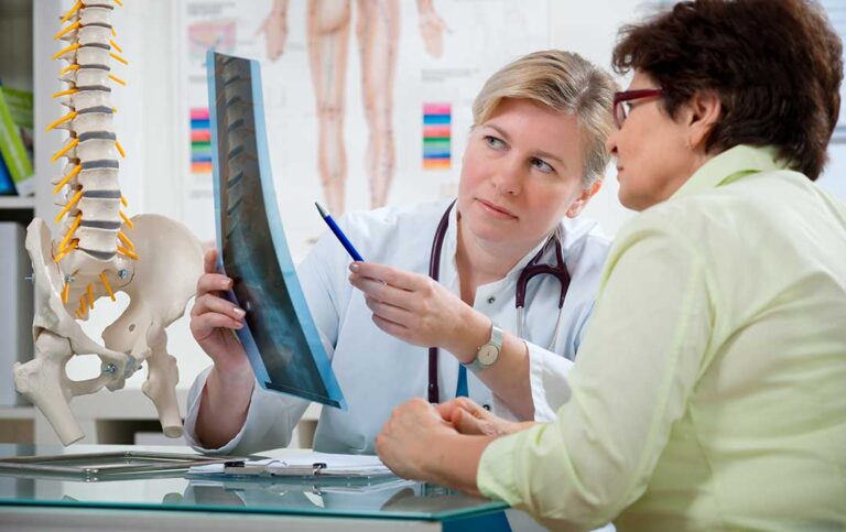 Adult performing gentle back exercises on a mat beside a clinician in a bright treatment room.
