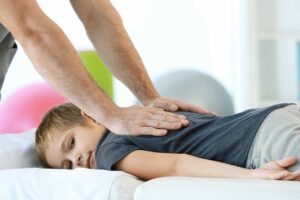 Clinician performing a gentle spinal adjustment on an adult patient in a bright examination room.