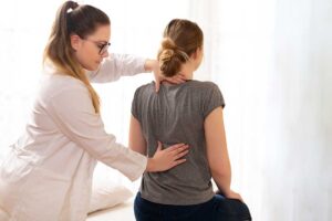 Patient discusses back pain with a healthcare provider beside an anatomical spine model.