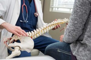 Patient in comfortable clothing discusses back symptoms with a chiropractor beside an examination table.